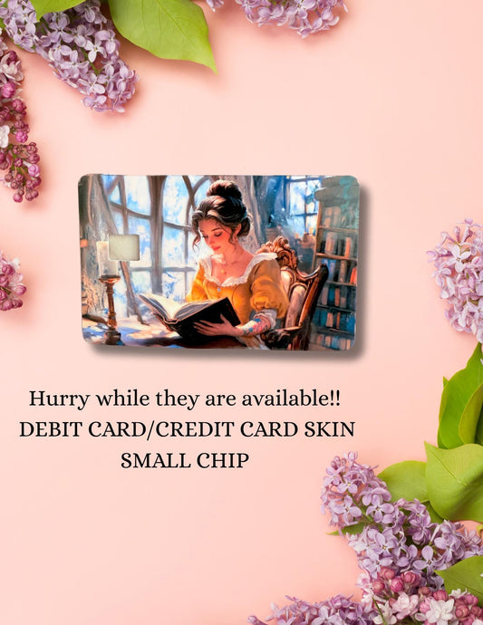 An Etsy product listing image featuring a debit card skin with an illustration of a woman in a yellow dress reading a book in a cozy, book-filled room. The card is centered on a peach background adorned with purple lilacs. Below the card, the text reads: &quot;Hurry while they are available!! DEBIT CARD/CREDIT CARD SKIN SMALL CHIP.&quot; The scene conveys a romantic, literary aesthetic.
